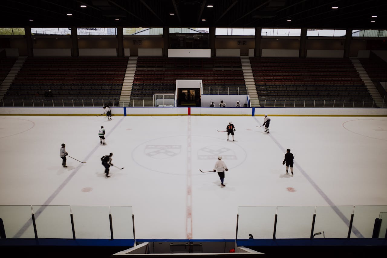 A group of ice hockey players practicing in an indoor rink with empty stands in the background.