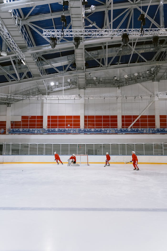Ice hockey players in red uniforms practice on the ice rink inside a large stadium.